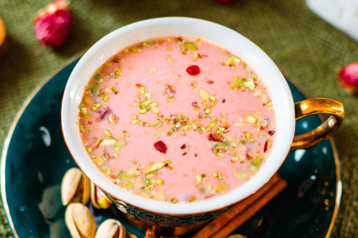 kashmiri pink chai in teacup surrounded by flowers, spices.