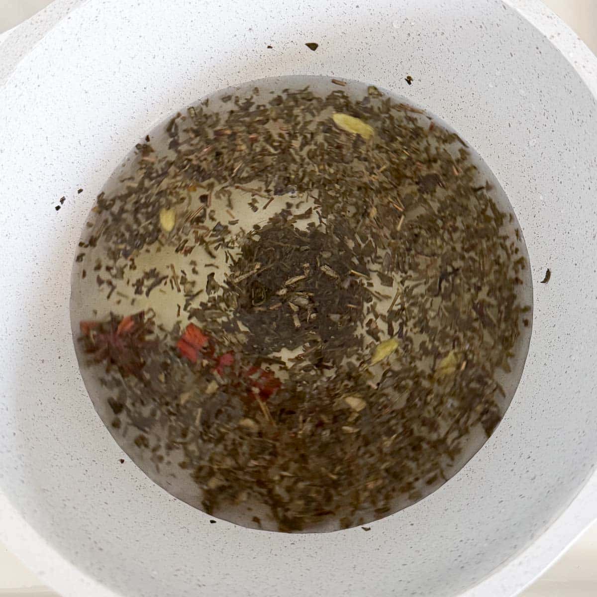 tea leaves and spices in water in pot.