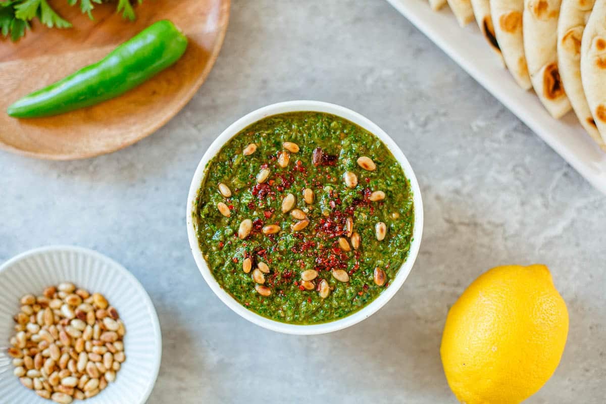 green harissa with pine nuts surrounded by lemon, nuts, pita, green pepper, herbs.