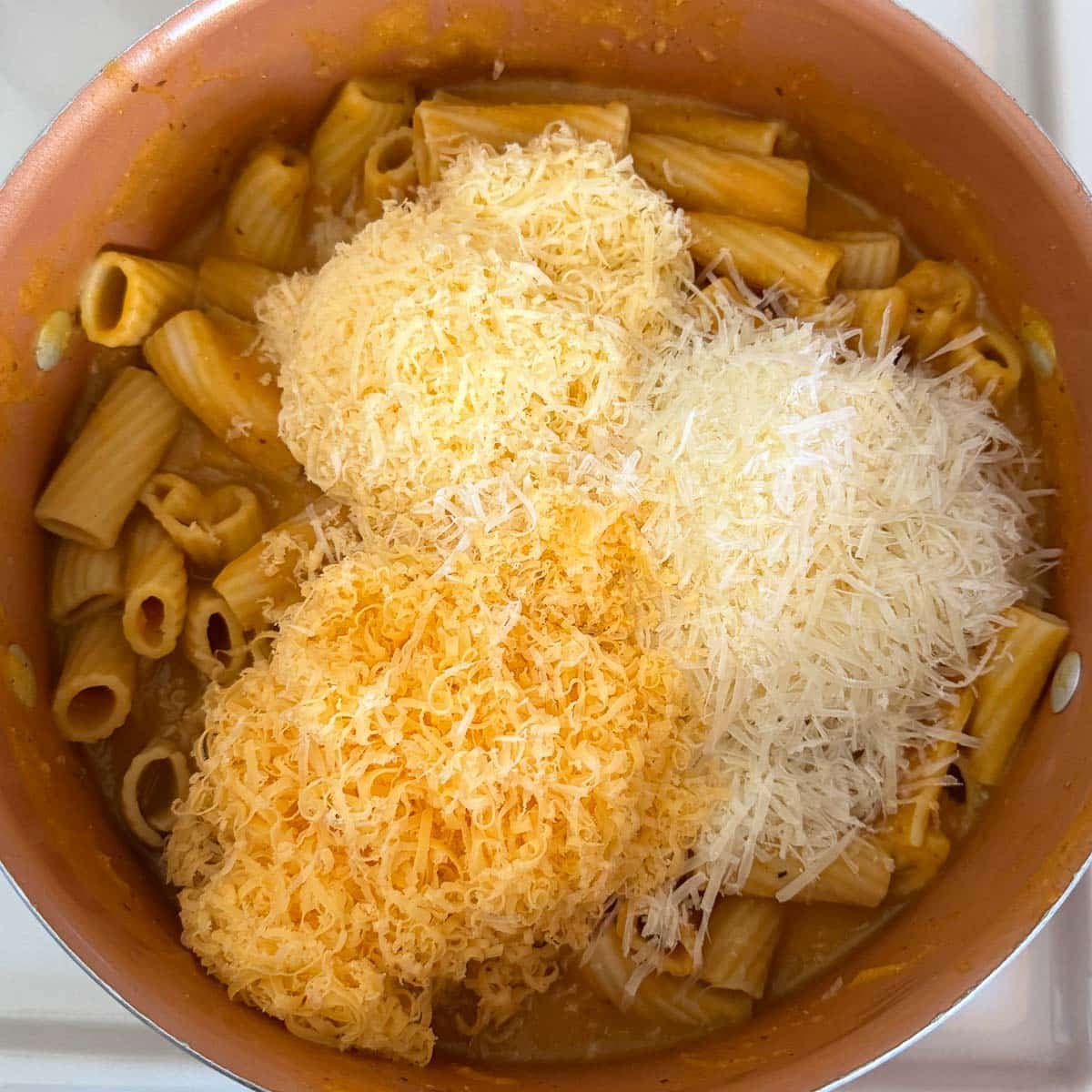 three piles of shredded cheese (cheddar, parmesan, gouda) atop pasta.