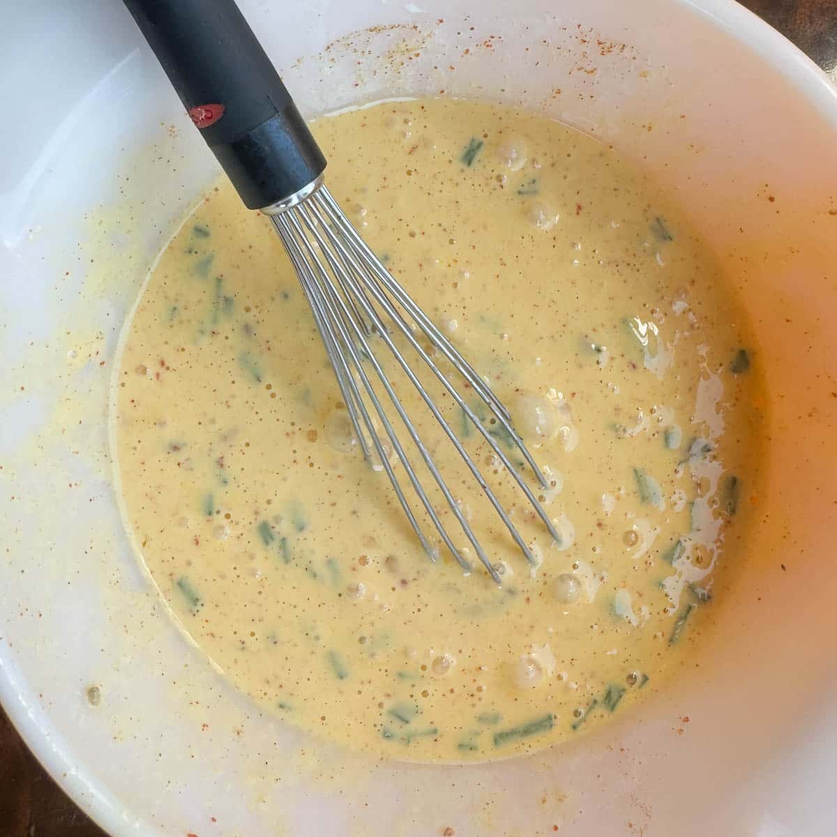 egg batter with herbs in a dish with a whisk. 