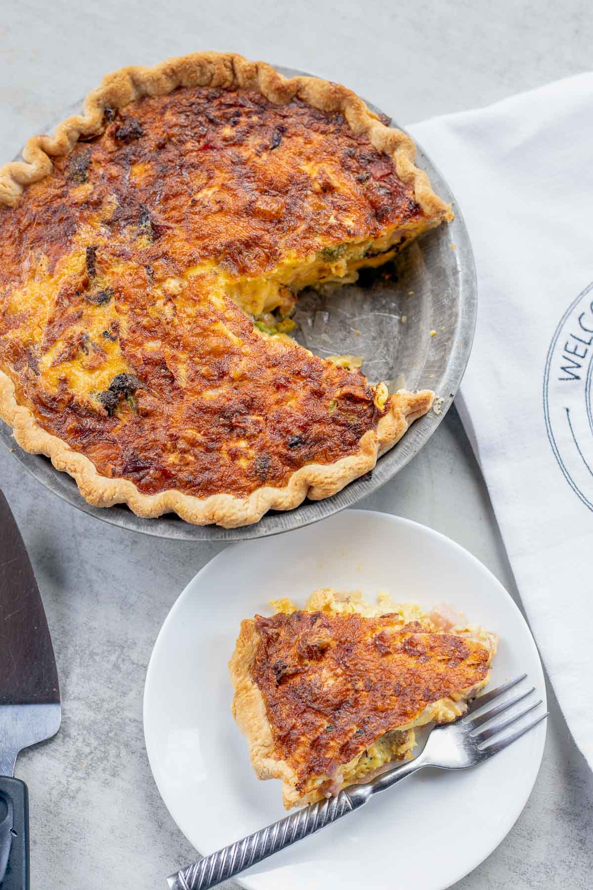 air fryer quiche with a piece removed on a white dish next to it. 