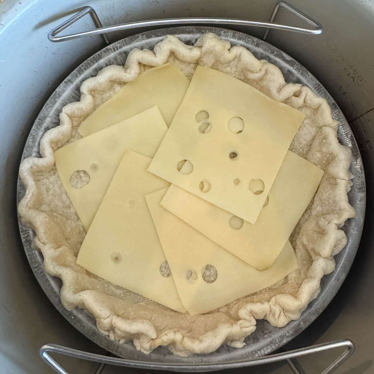 unbaked pie shell with swiss cheese slices. 