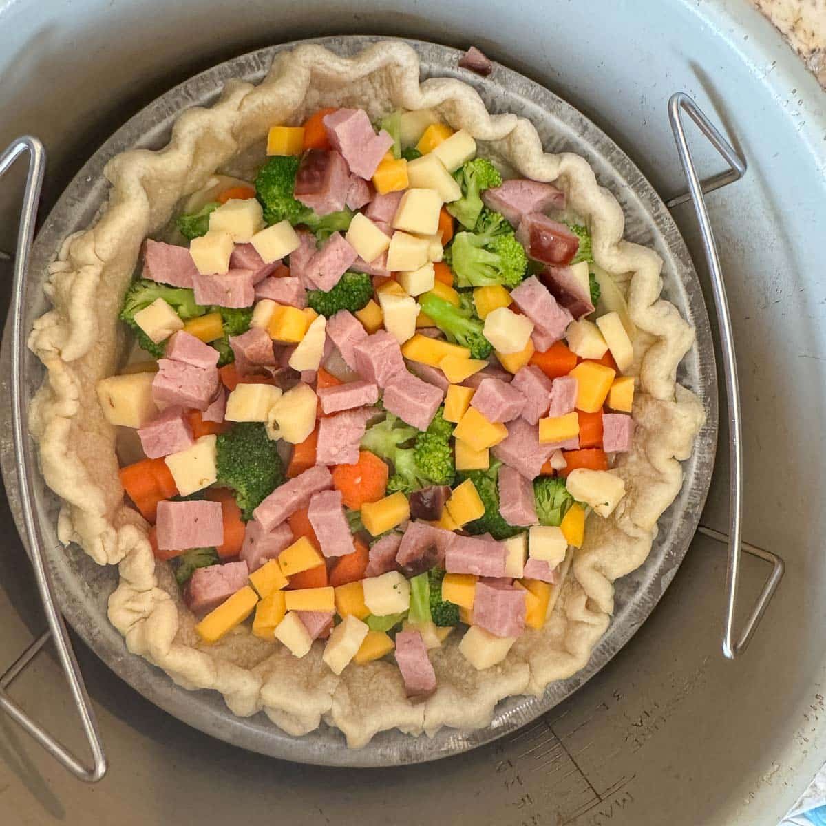 pie shell in air fryer filled with chopped veggies, meat, and cheese.
