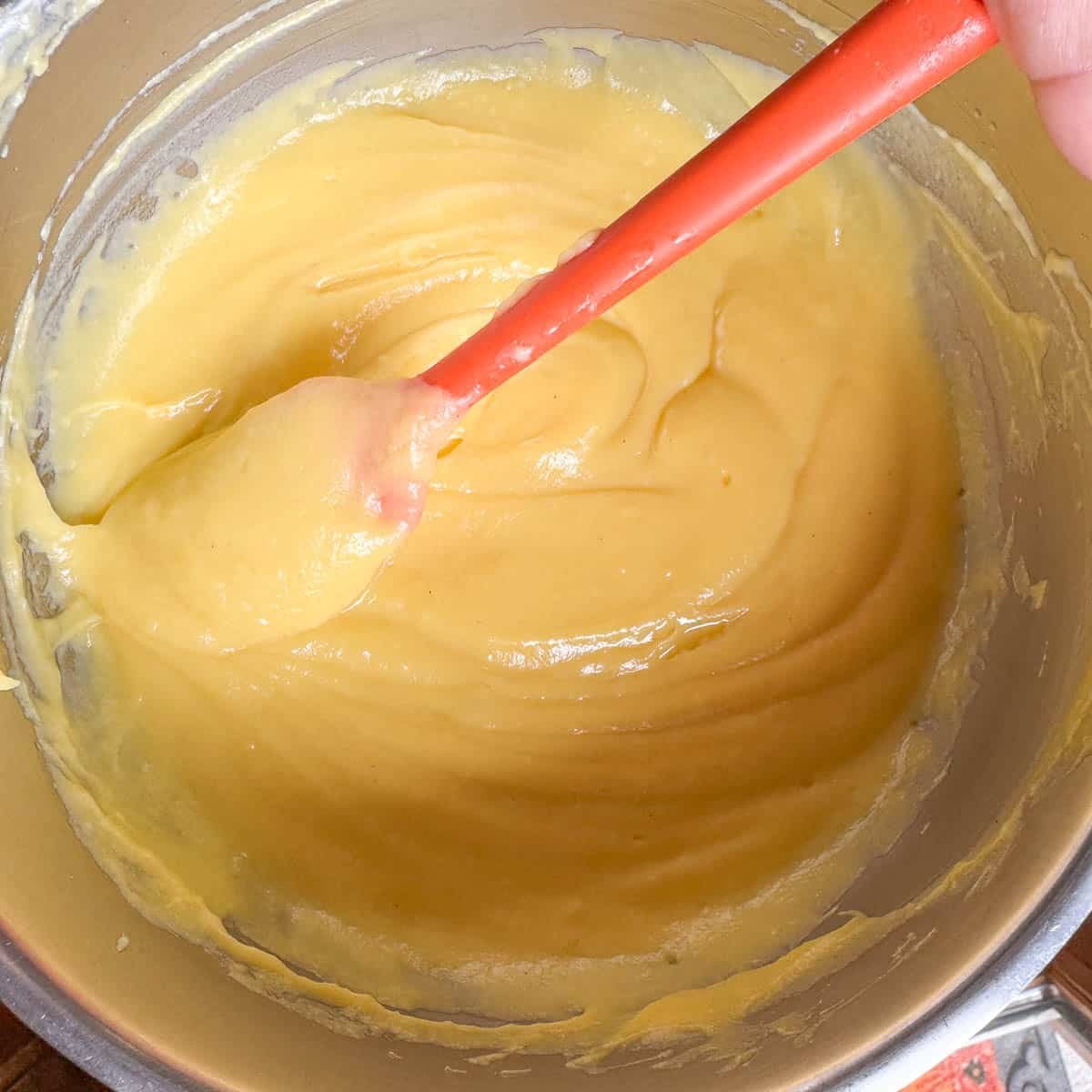 custard in a silver bowl with an orange spatula. 