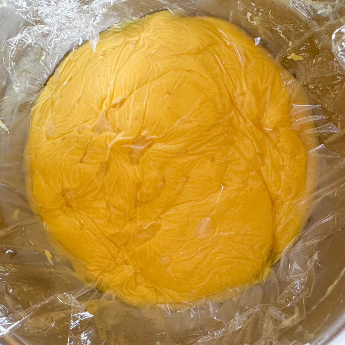 custard in a silver bowl  covered with plastic wrap. 