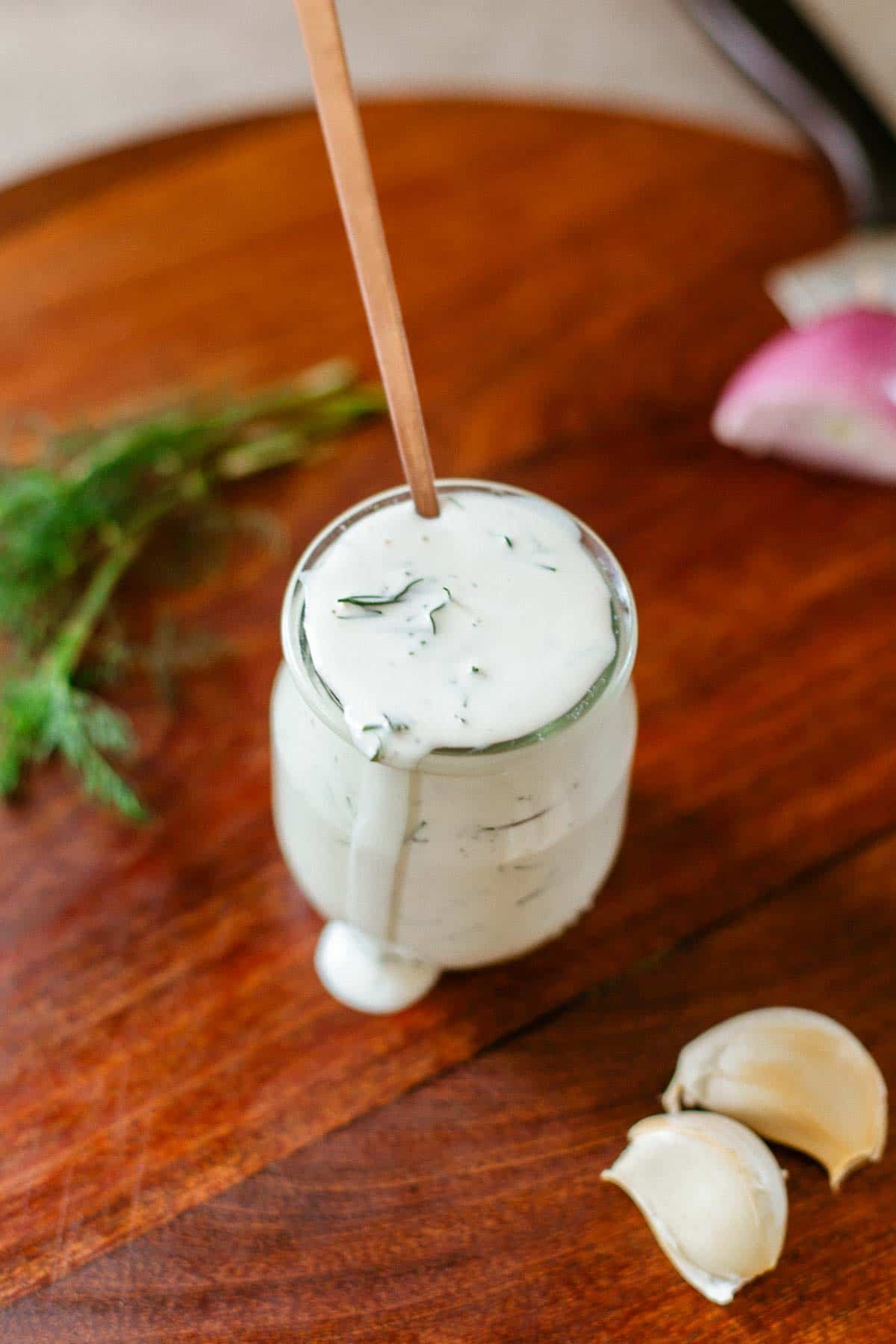 jar of dill salad dressing with spoon beside herbs and aromatics.