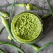garlic scape pesto in a jar with more scapes around it.