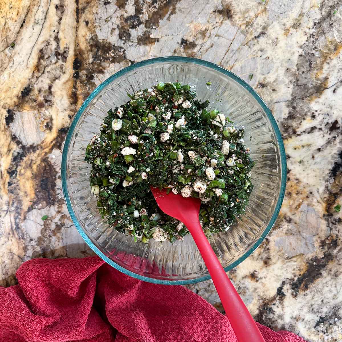 stirring spinach feta toppings in a bowl with a red spatula.