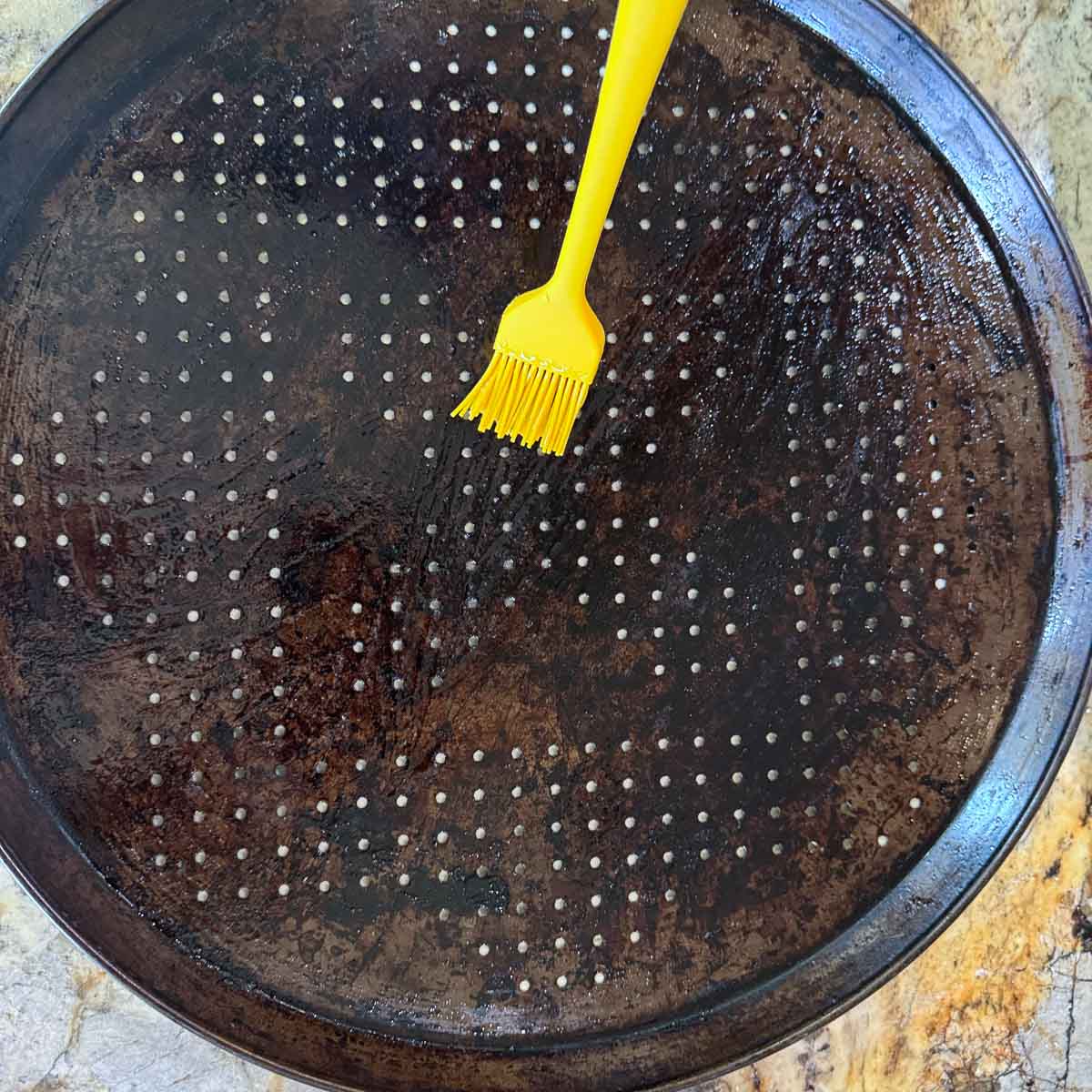 brushing a pan with oil using a yellow pastry brush.