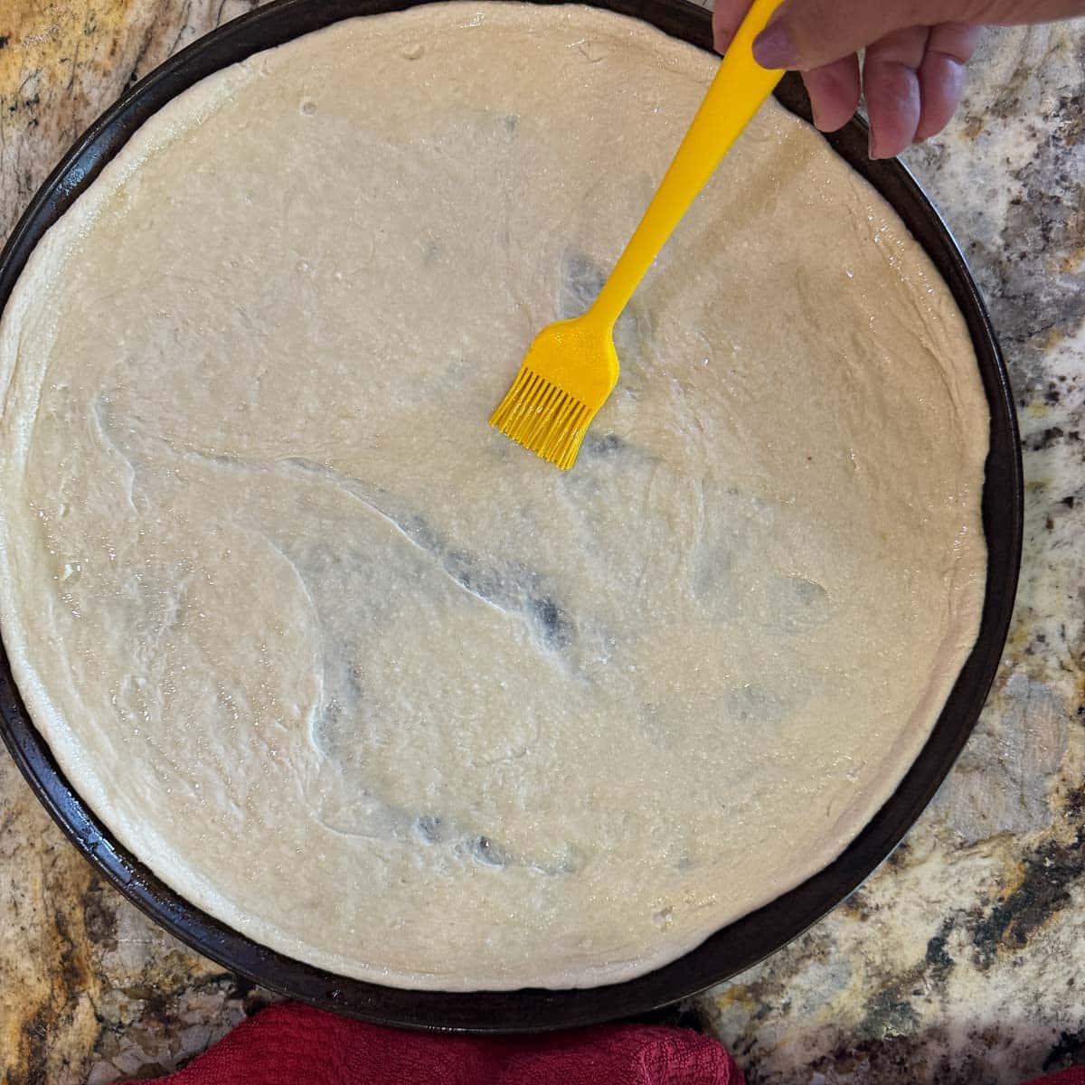 brushing pizza dough with toum using a yellow pizza brush.