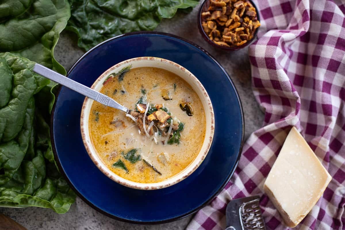 swiss chard soup in a blue plate with  swiss chard, cheese, and bacon on the side. 