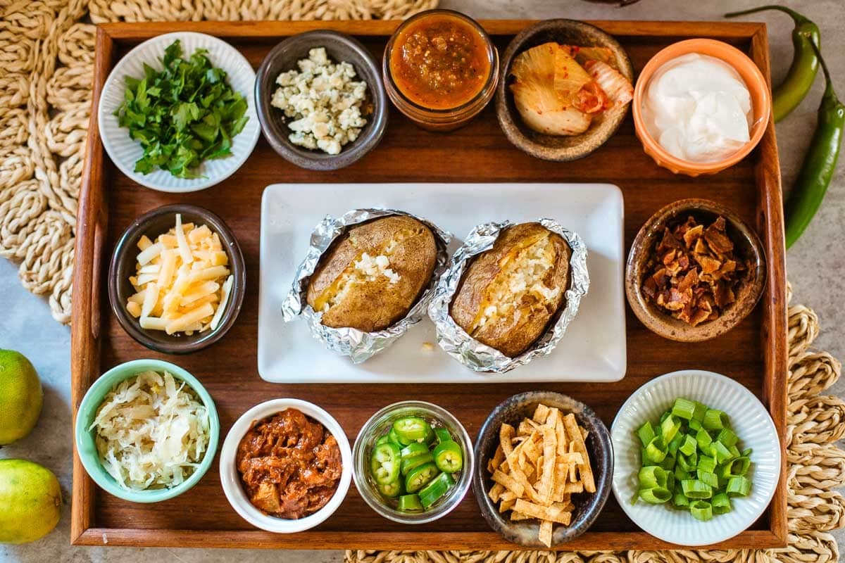 baked potatoes surrounded by bowls of various toppings and mix-ins.