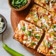 bbq chicken flatbread cut into slices surrounded by various toppings.