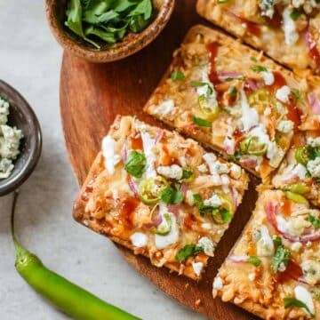 bbq chicken flatbread cut into slices surrounded by various toppings.