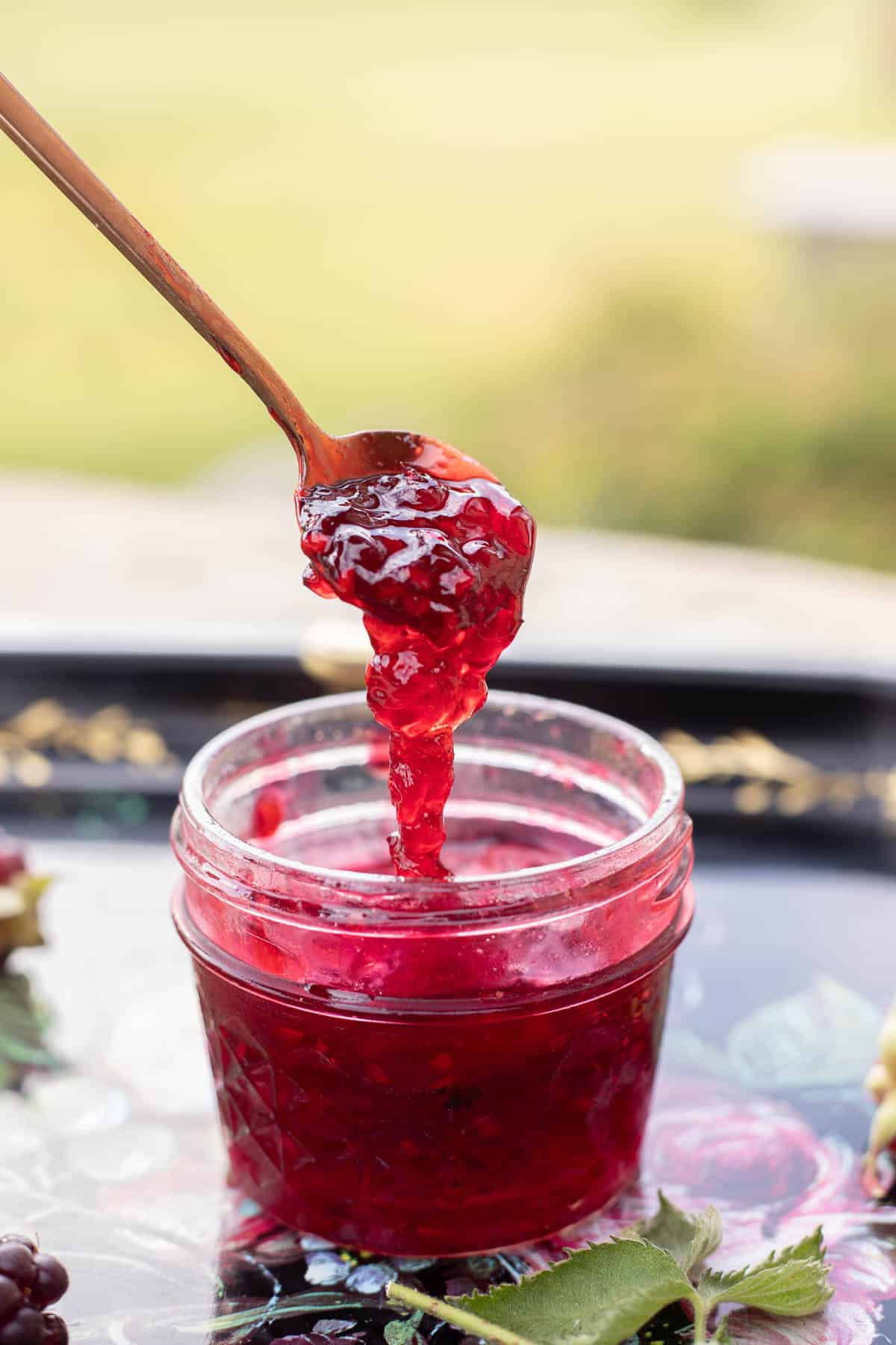 a spoon full of boysenberry jam spilling into the jar. 
