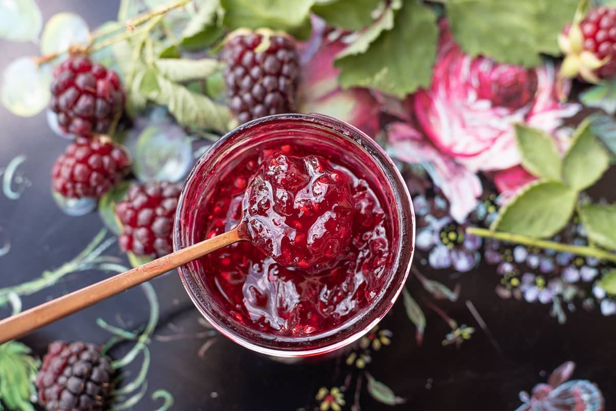 boysenberry jam on a colorful background with boysenberries around the jar.