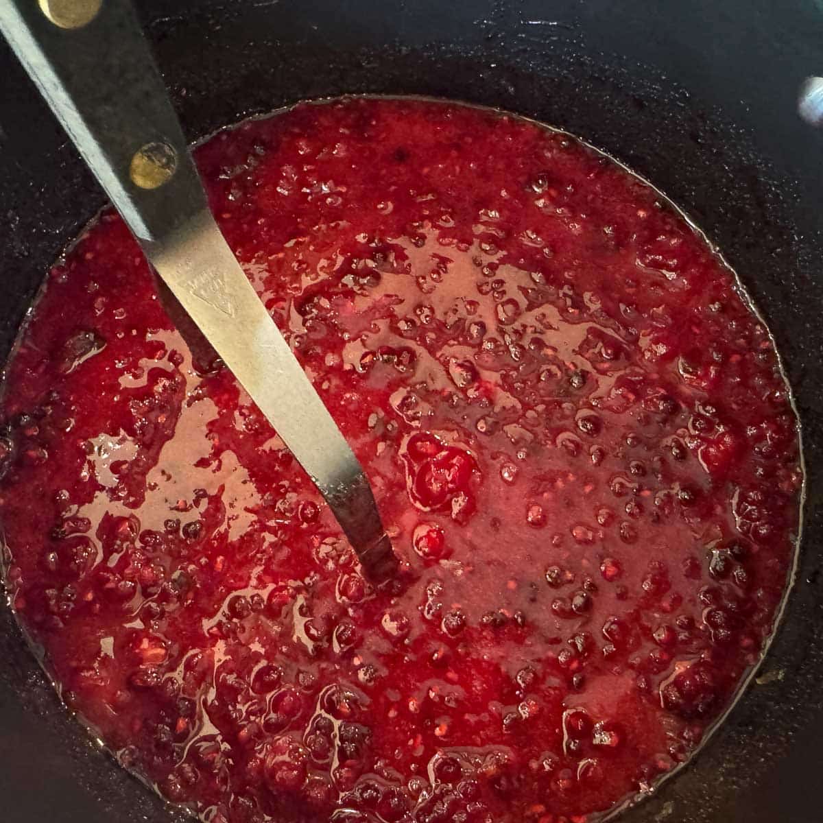 mashing boysenberries in a pot of boysenberry jam.