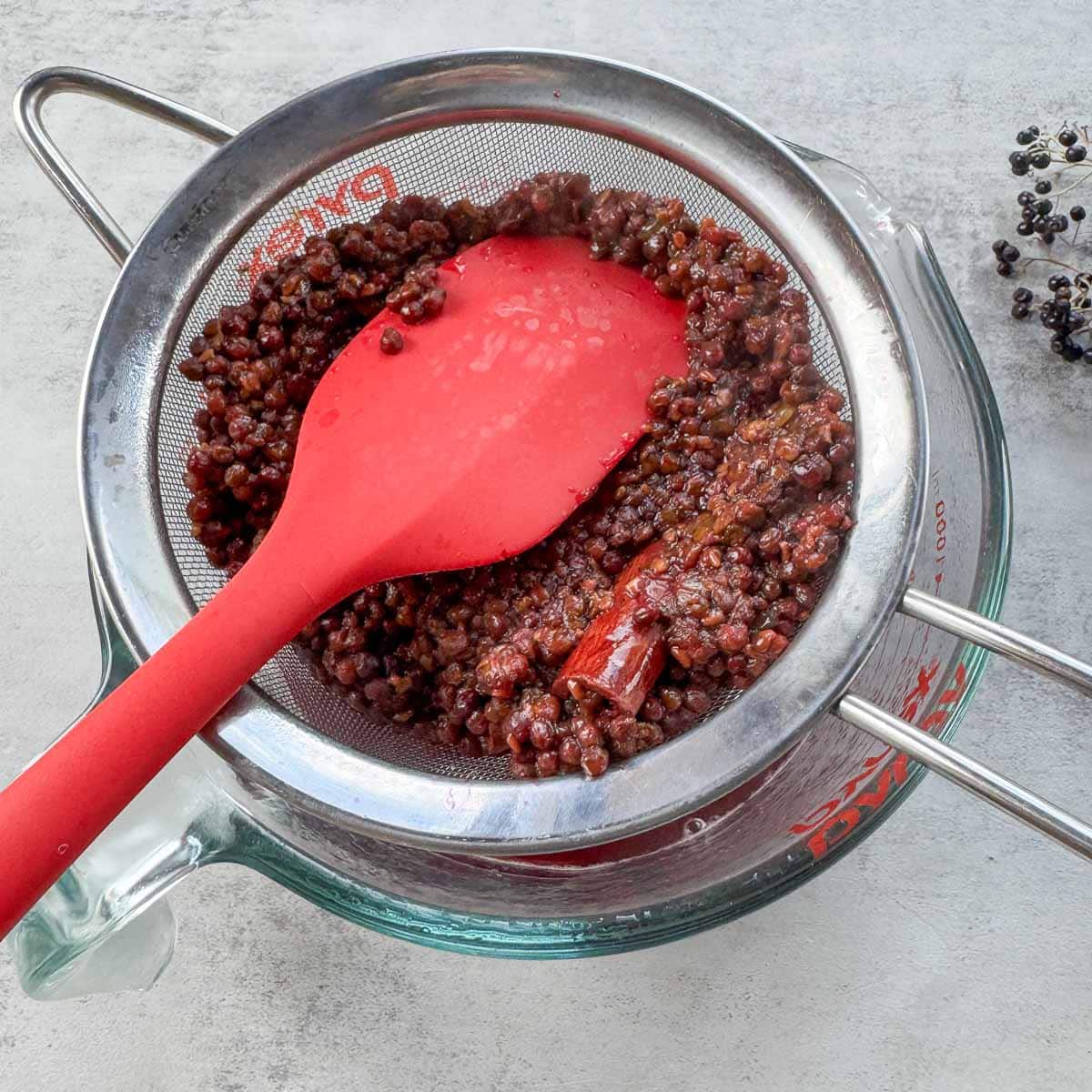 straining elderberry syrup into a cup.