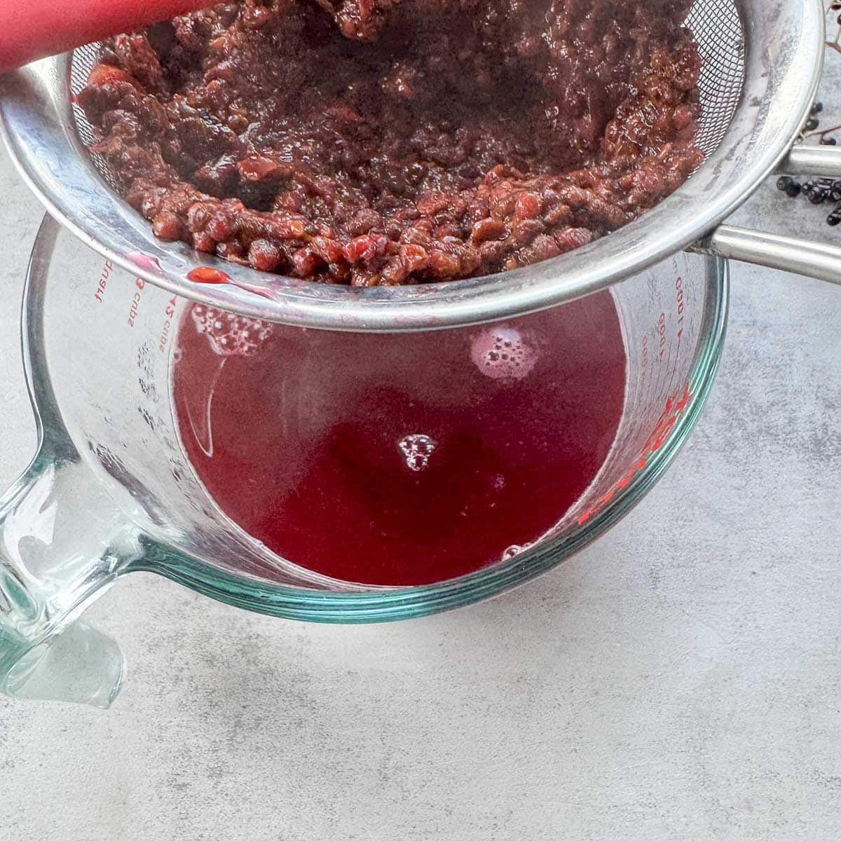 straining elderberry syrup into a large measuring cup. 