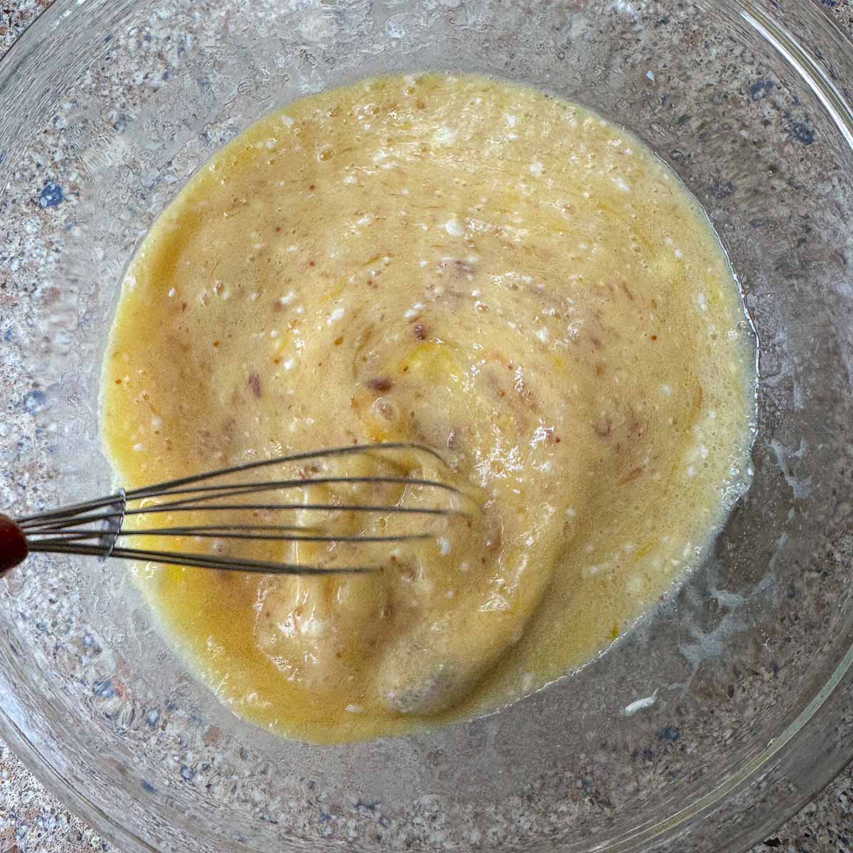 wet cake ingredients in a bowl being whisked. 