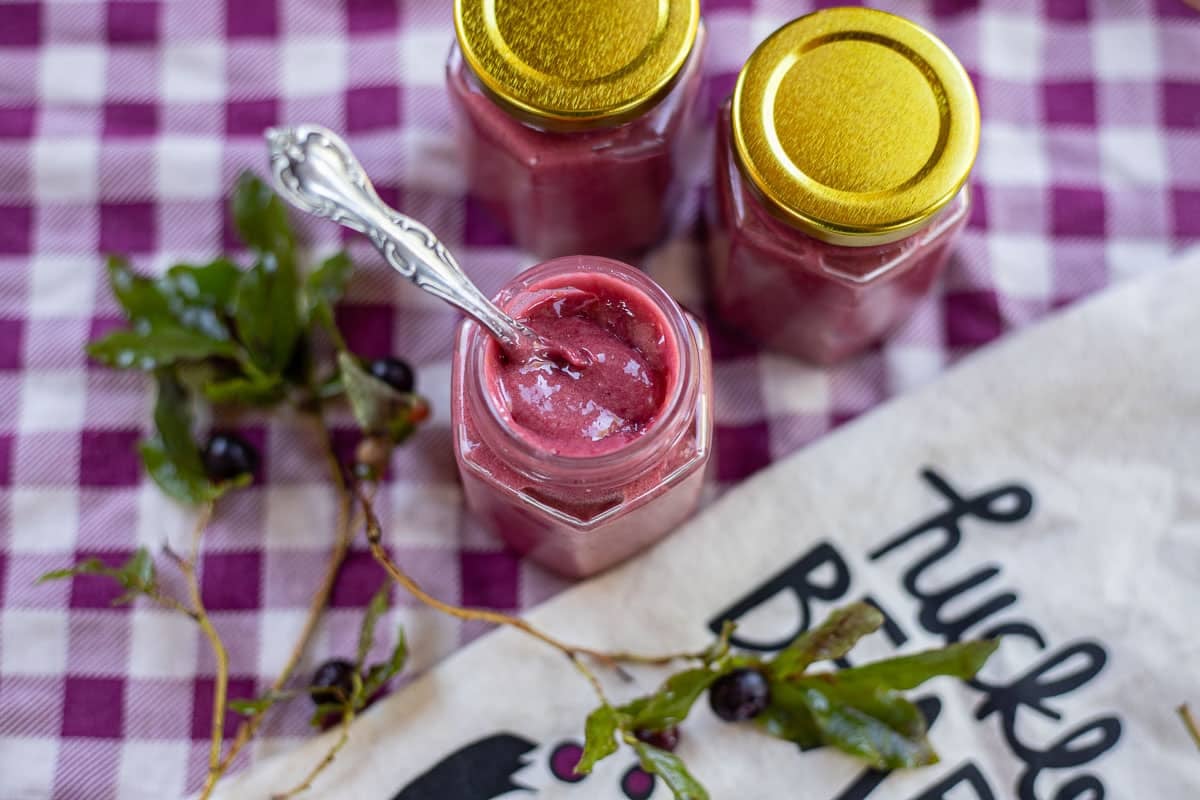 huckleberry curd in a jar with a few more jars behind it and huckleberries around it. 