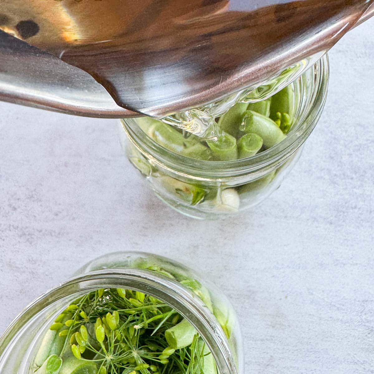 Brine being poured over jarred green beans. 