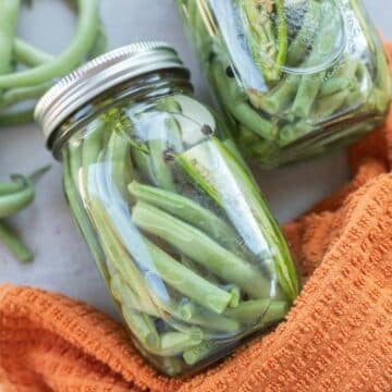pickled green beans in jars with more green beans net to it.