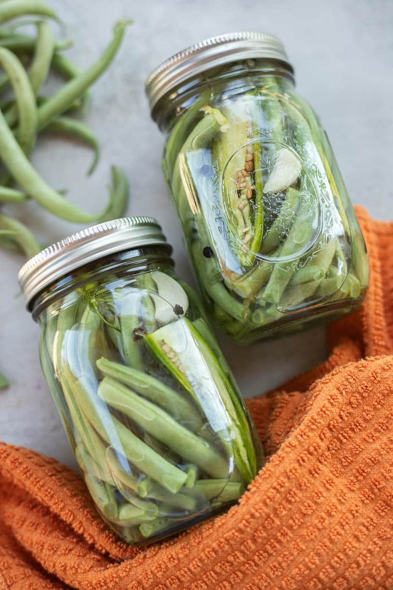 pickled green bean in a jar with green beans next to it. 