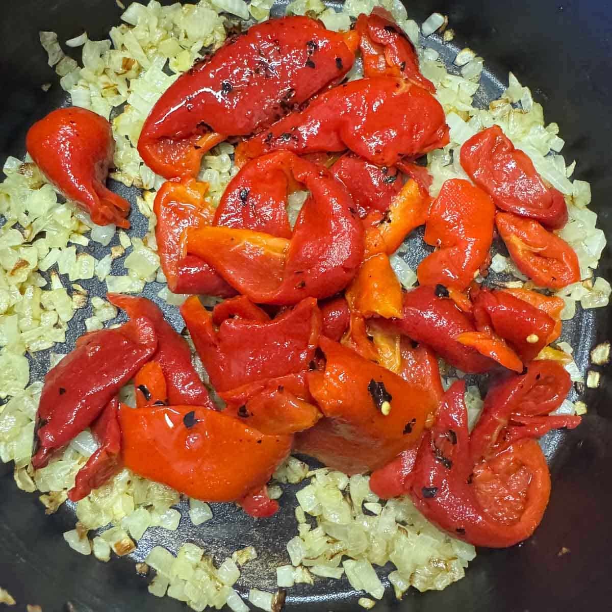 sauteed onions in a pot with roasted peppers on top.