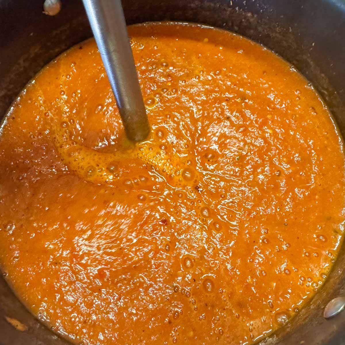 using immersion blender to blend tomato pepper soup.