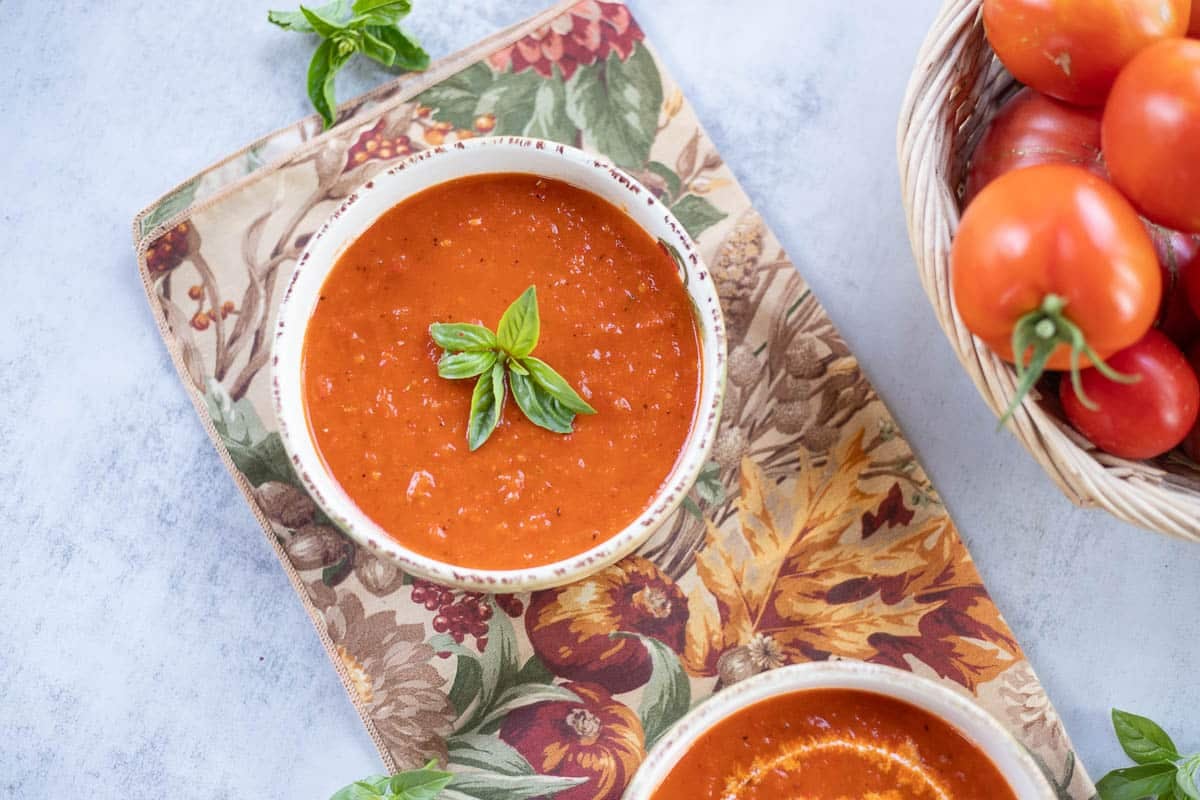 roasted tomato pepper soup in a bowl with a basket of tomatoes next to it.