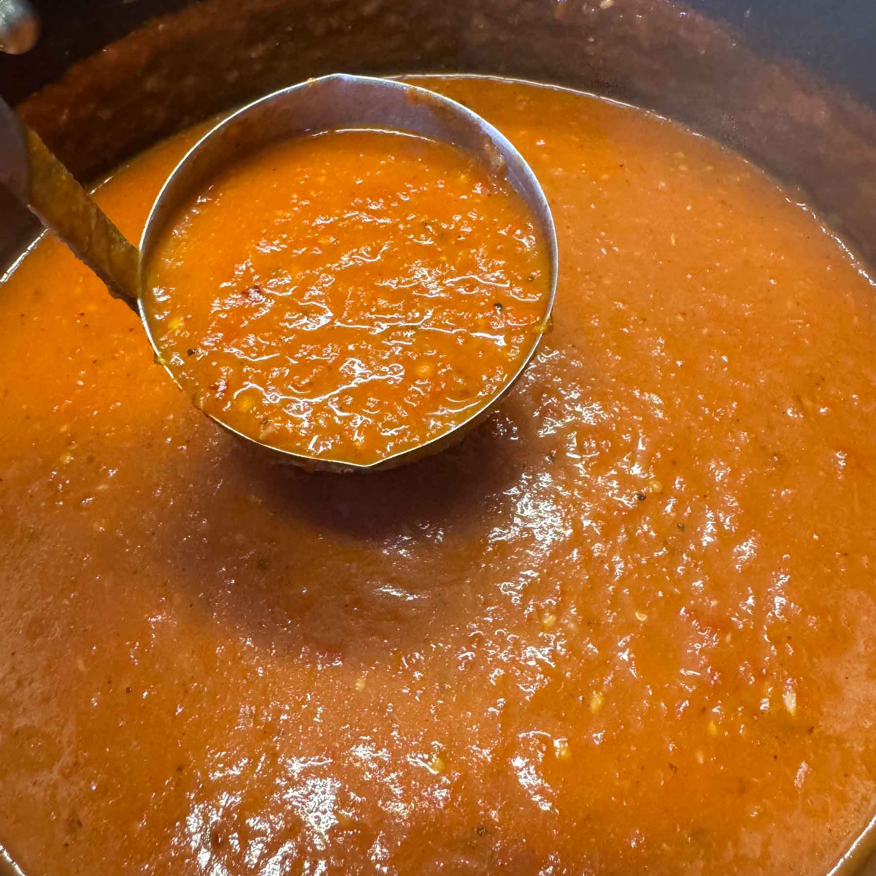 roasted tomato pepper soup in a ladle.