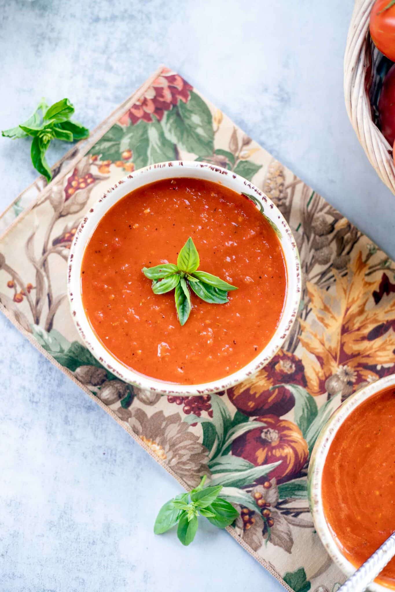 Smoky roasted tomato pepper soup garnished with basil with tomatoes and basil on the side.