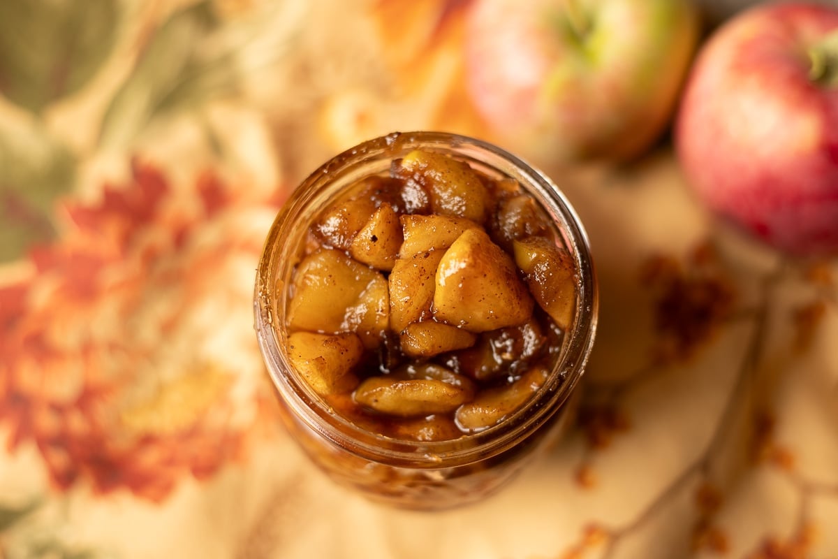 apple compote in a jar with apples next to it.
