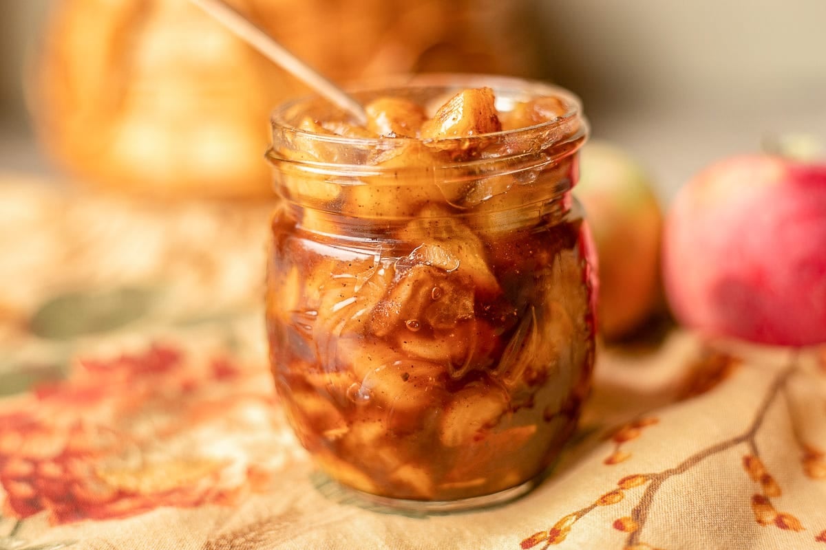 a jar of apple compote with apples behind it.