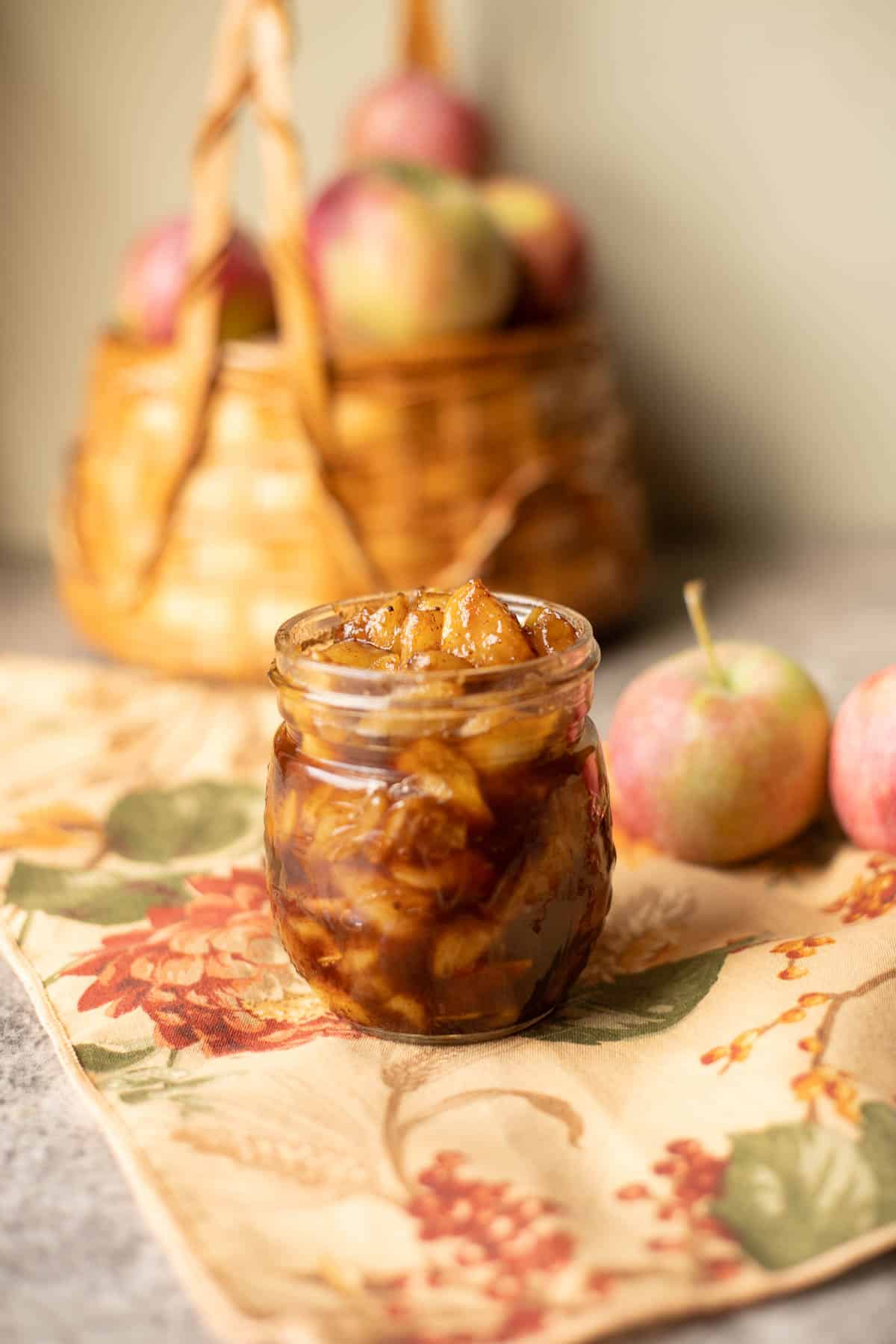 apple compote in a jar with a basket of apples behind it.