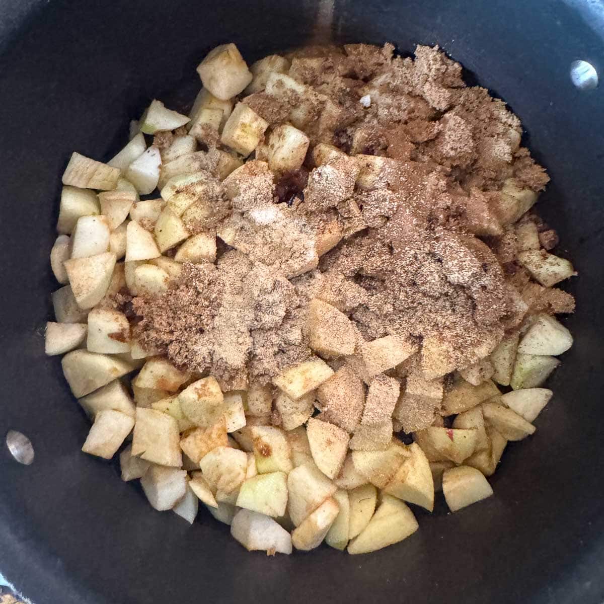 chopped apples in a pot topped with sugar and spices.
