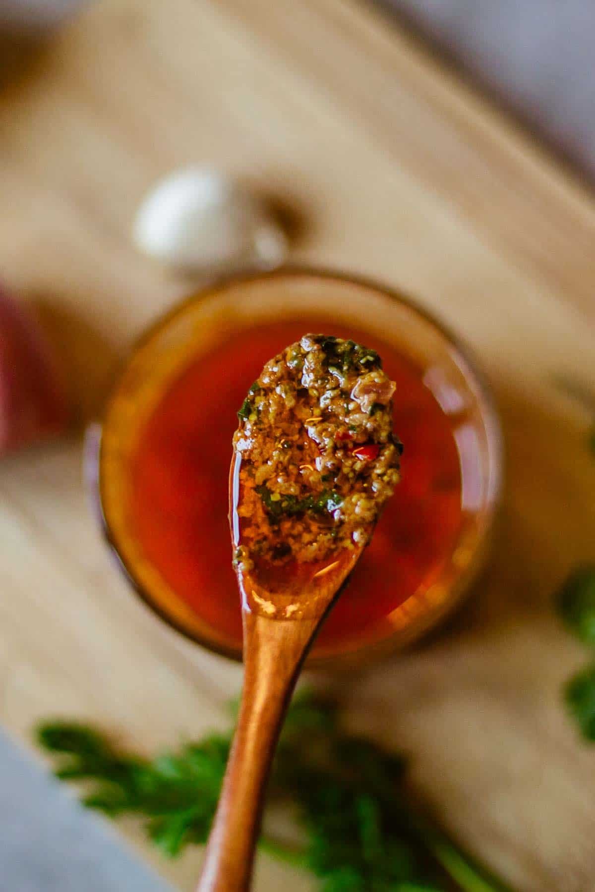 spoon of cowboy butter held over bowl beside herbs.