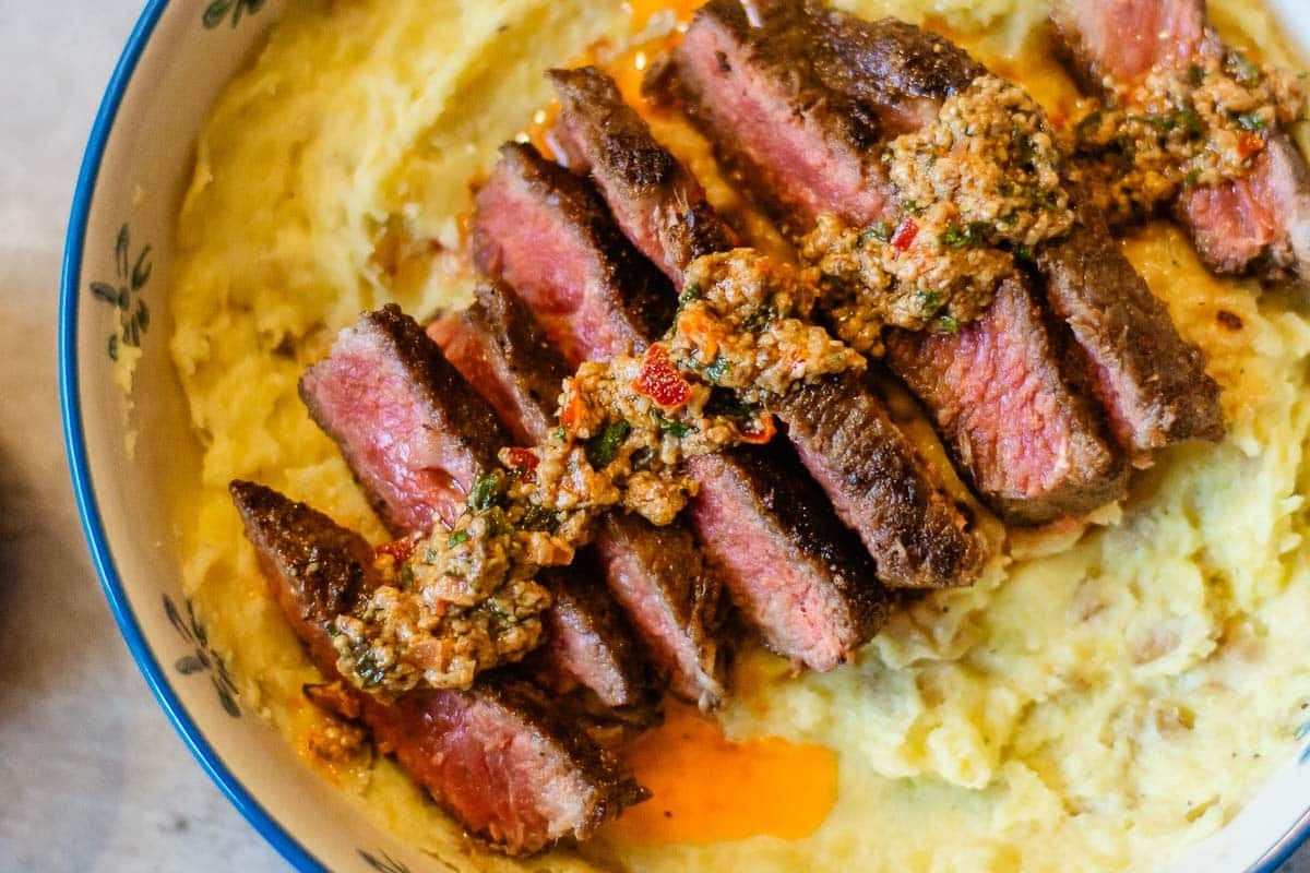cowboy butter drizzled over sliced steak over mashed potatoes.