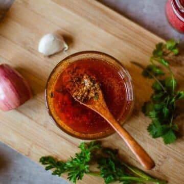 cowboy butter in bowl with spoon beside herbs, lemon, and pepper paste.