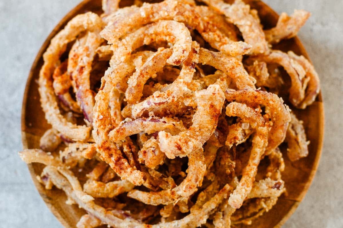 heaping pile of frizzled onions on wooden plate.