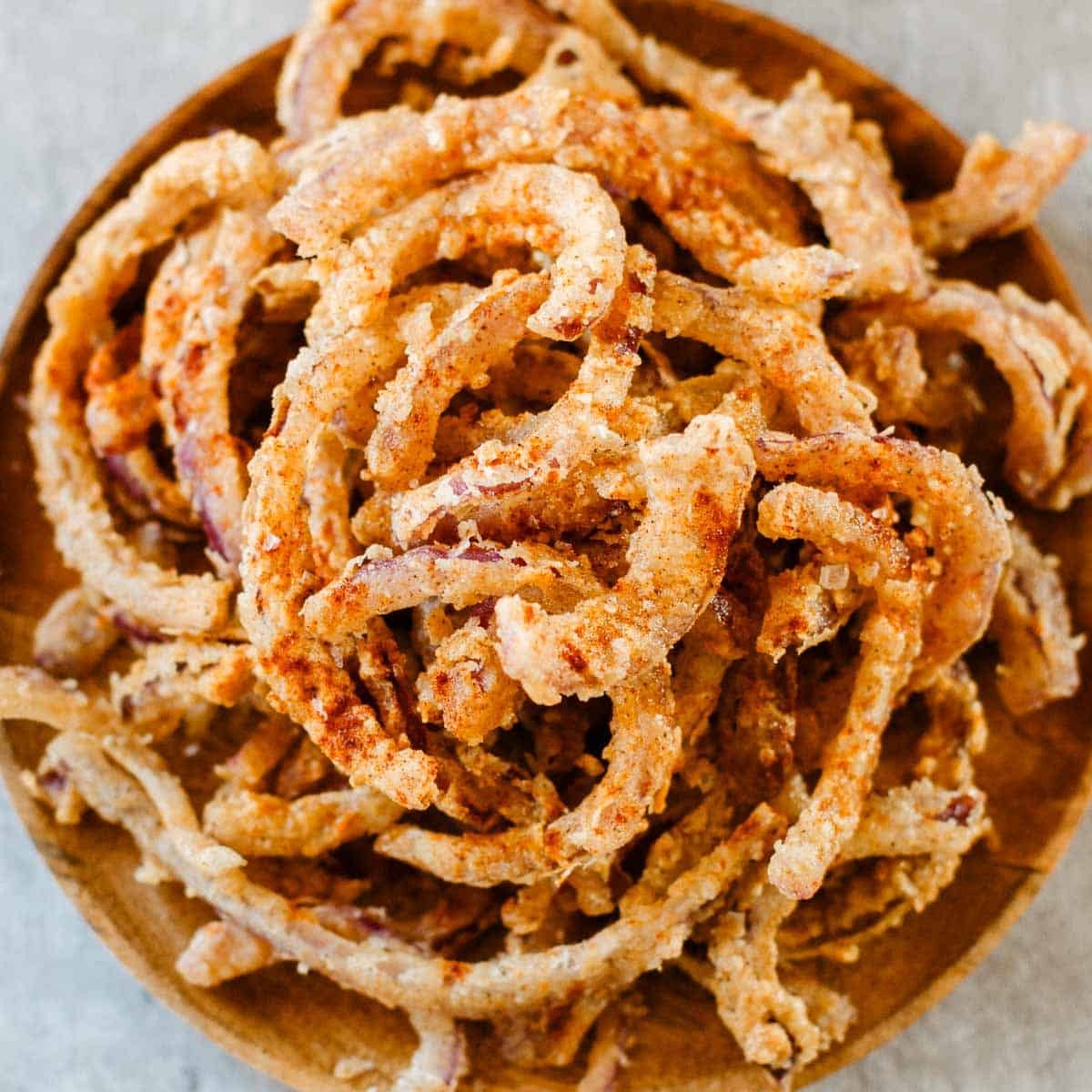 heaping pile of frizzled onions on wooden plate.