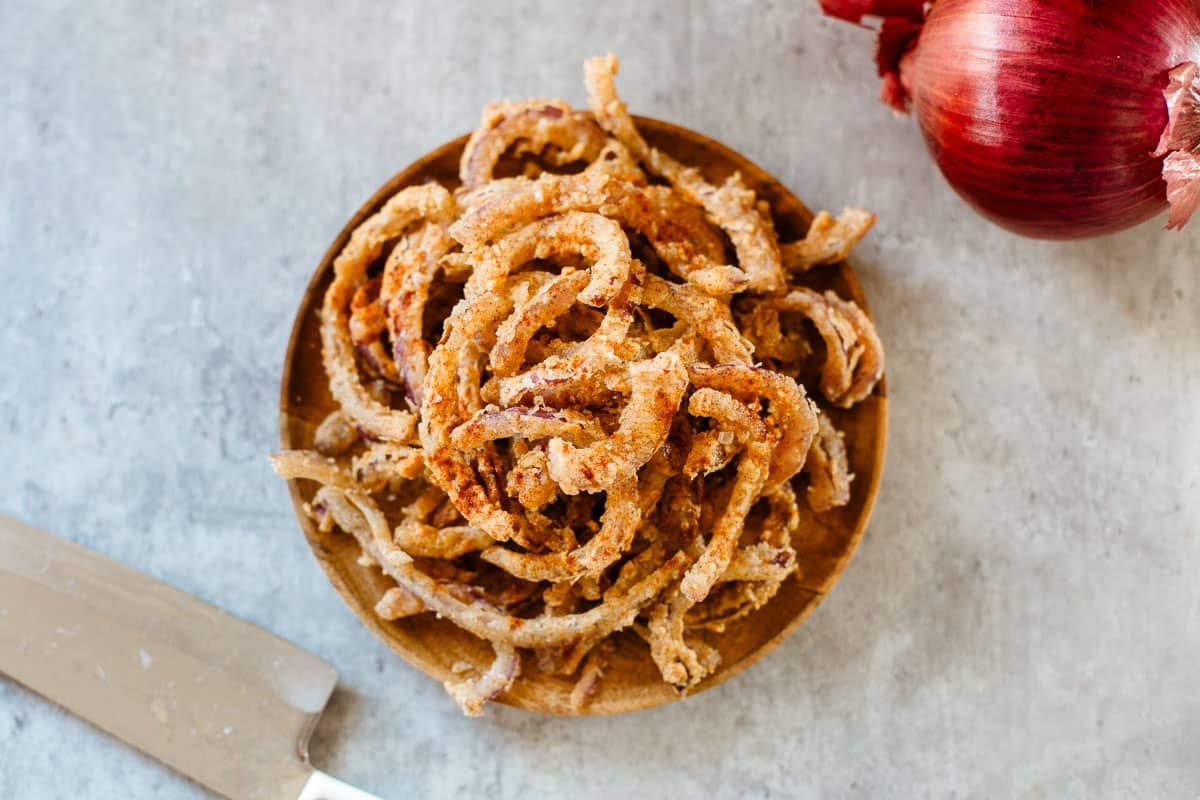 heaping pile of frizzled onions on wooden plate.