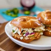 hot honey chicken sandwiches on plate beside chopped onions and jalapenos.