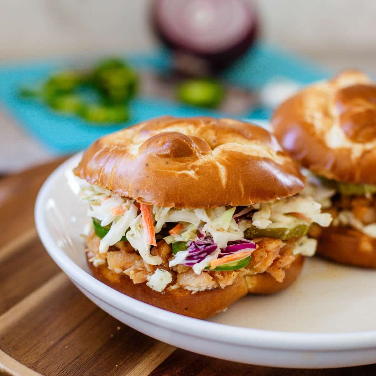 hot honey chicken sandwiches on plate beside chopped onions and jalapenos.