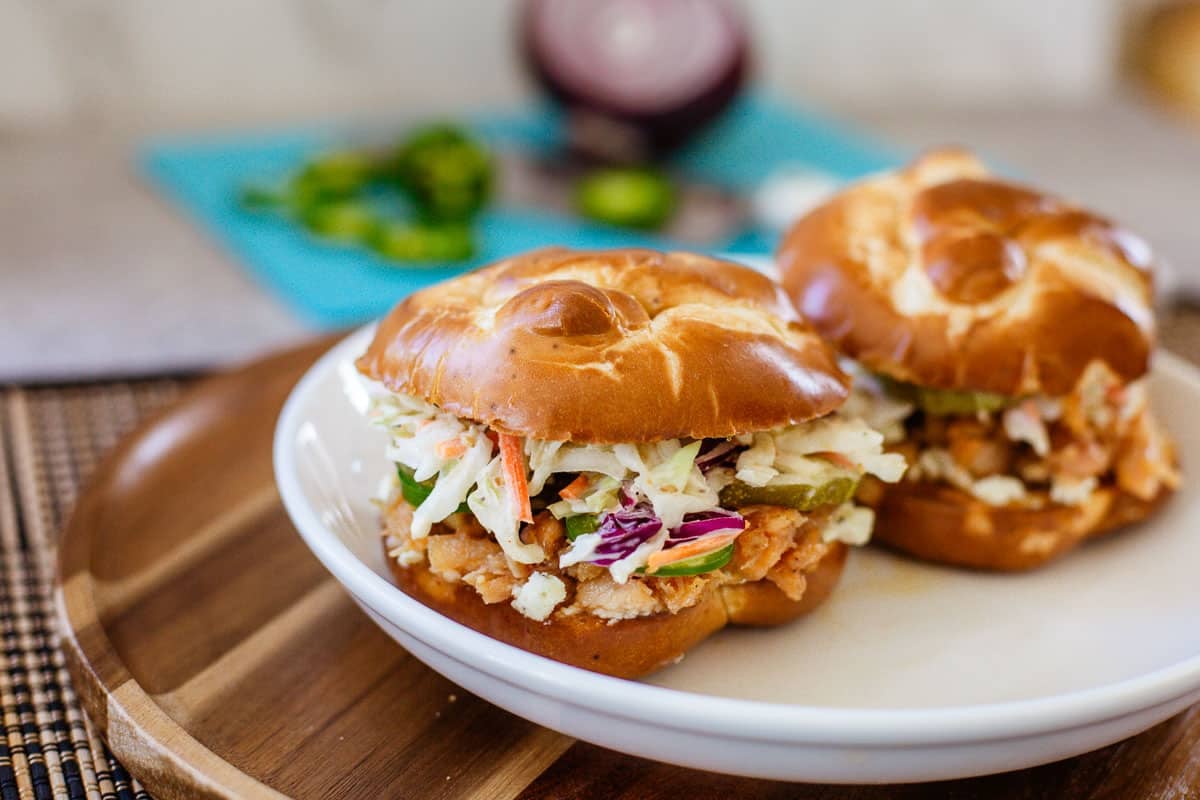 hot honey chicken sandwiches on plate beside chopped onions and jalapenos.