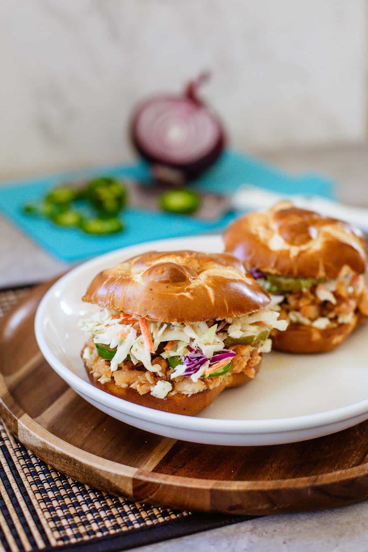 hot honey chicken sandwiches on plate beside chopped onions and jalapenos.