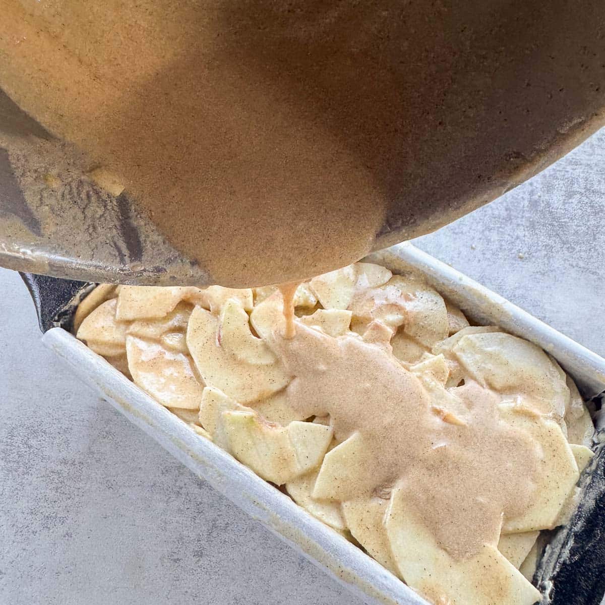 pouring batter over apple slices for an invisible apple cake. 