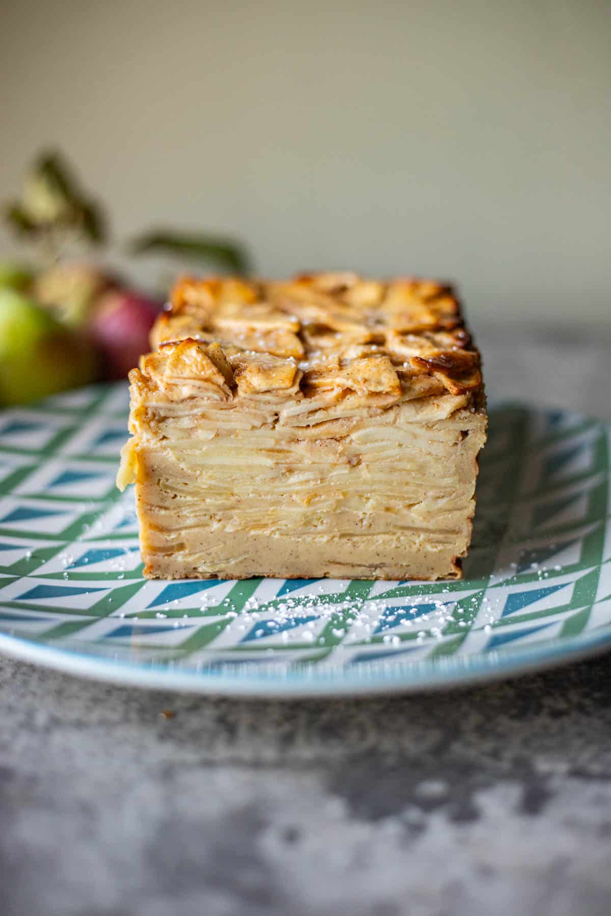 invisible apple cake on a blue and green plate with apples behind it. 
